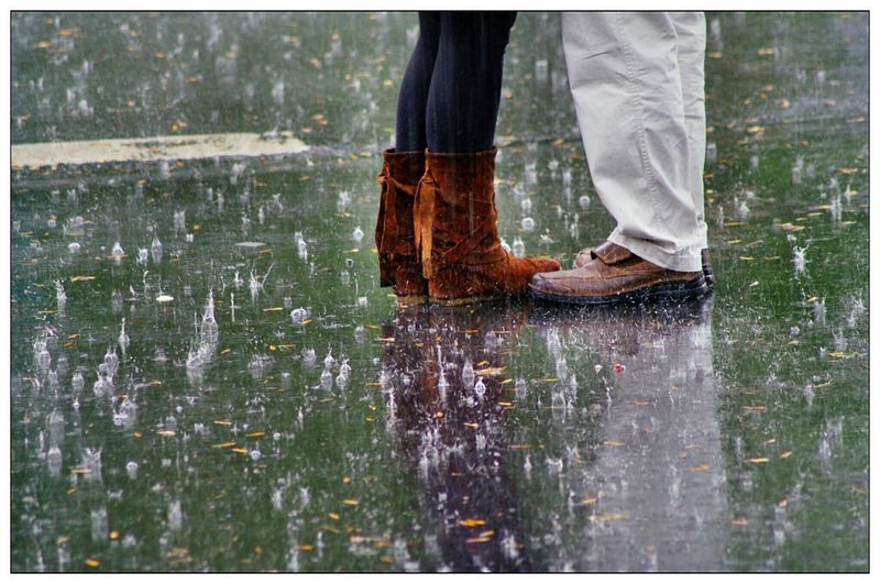 Low section of man and woman wearing shoes while standing on road during rainy season