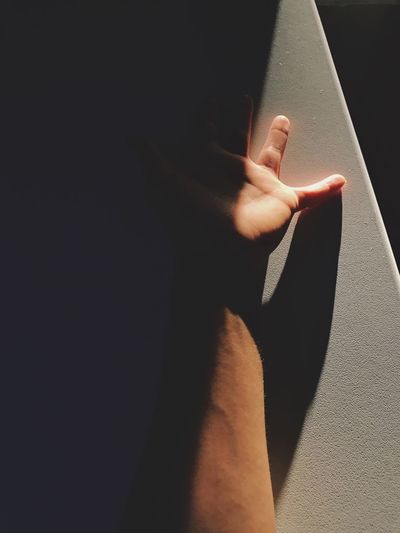 Sunlight falling on cropped hand against wall