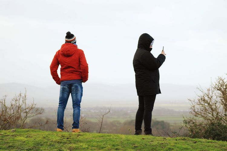 People standing on grassy field against sky during foggy weather