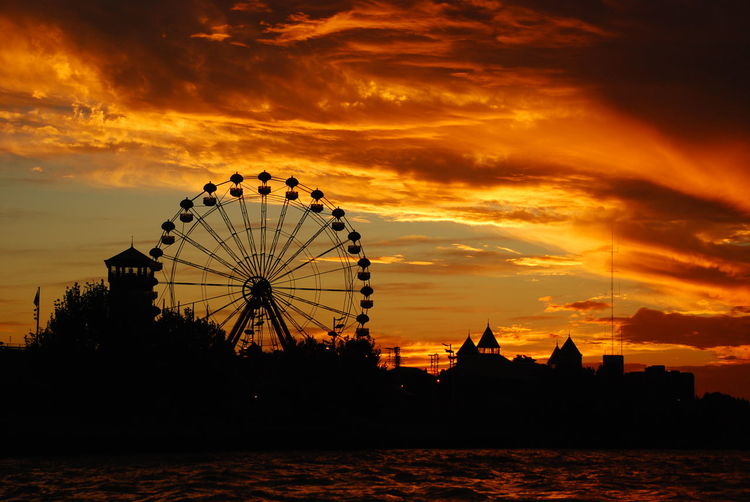 Silhouette of ferris wheel against cloudy sky during sunset