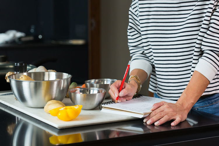 Woman checking recipe and ingredients in her notebook while cooking pie in the modern kitchen