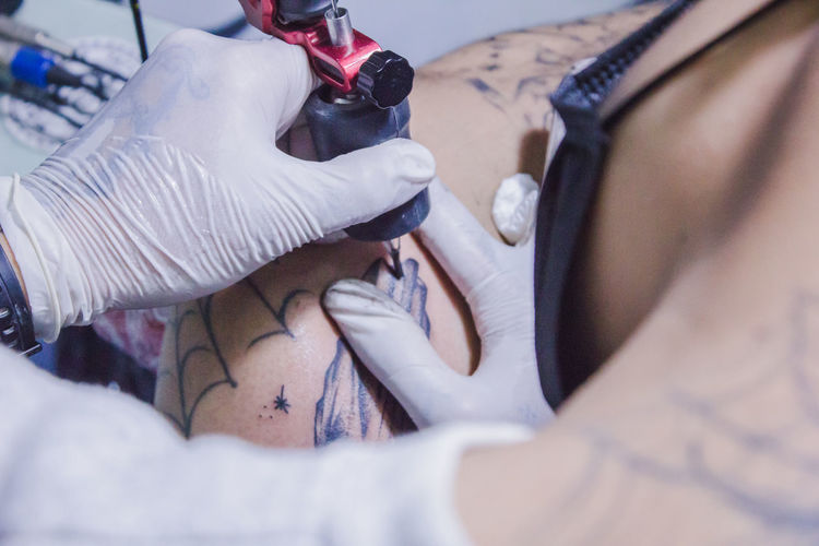 Cropped hands of artist making tattoo on man stomach