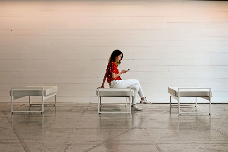Woman sitting on chair against wall