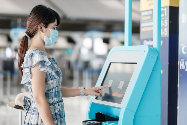 Side view of woman wearing mask using atm machine at airport