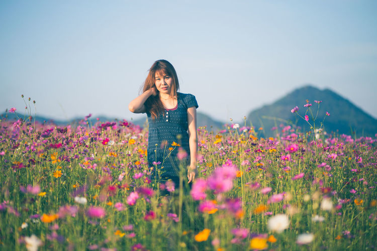 Woman standing amidst flowering plants on field against sky