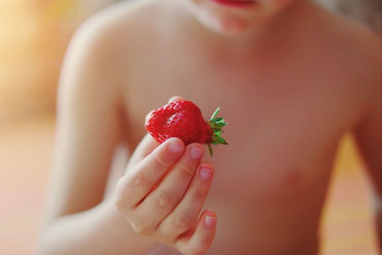 Midsection of shirtless boy holding strawberry