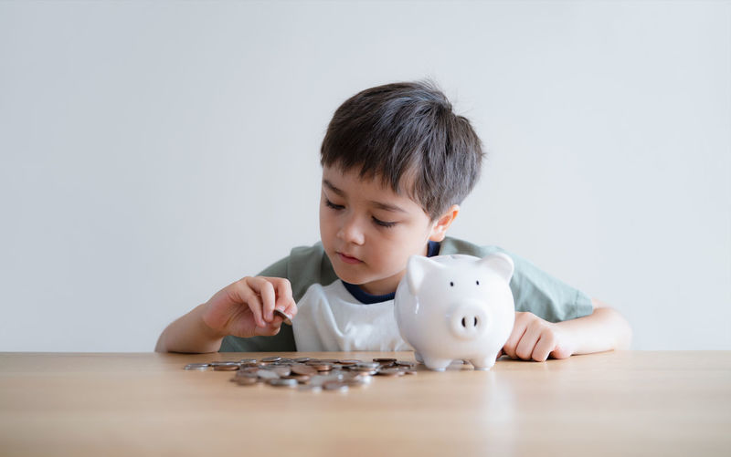 Portrait of smiling boy with piggy bank on table