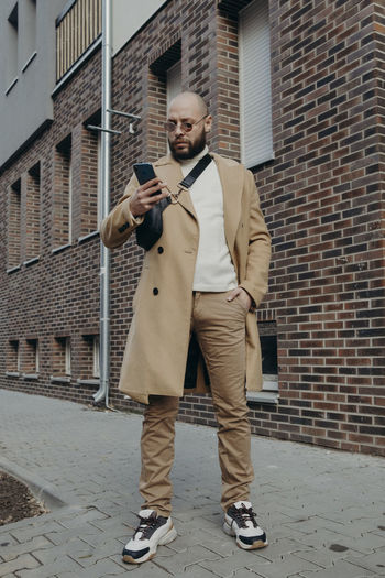 Full length of young man using mobile phone against brick wall