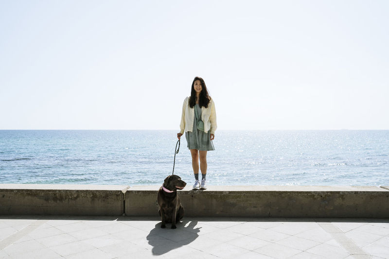 Woman with dog on sea against sky