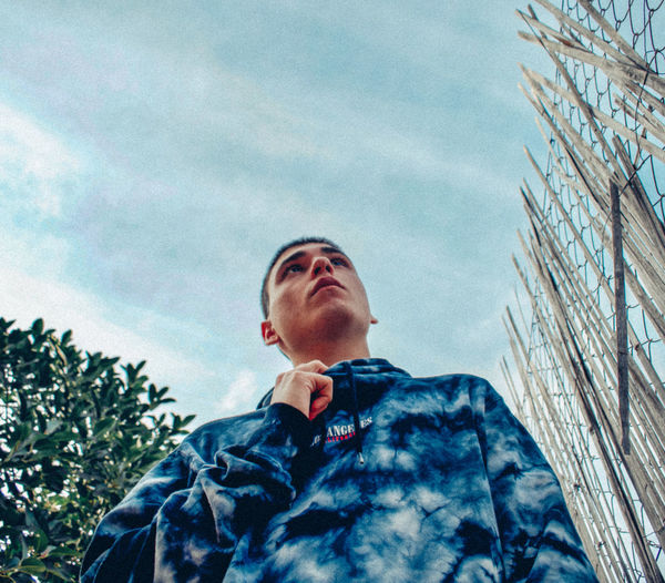 Low angle view of young man looking up against sky
