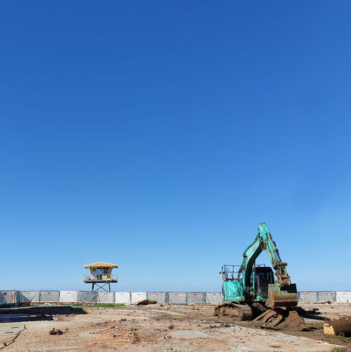 Scenic view excavator on beach against clear blue sky