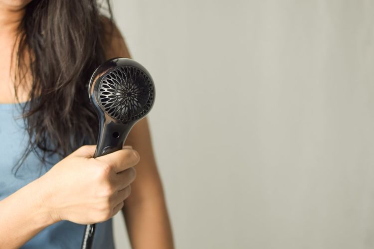 Midsection of woman holding hair dryer against white background
