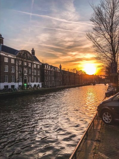 Canal by city against sky during sunset