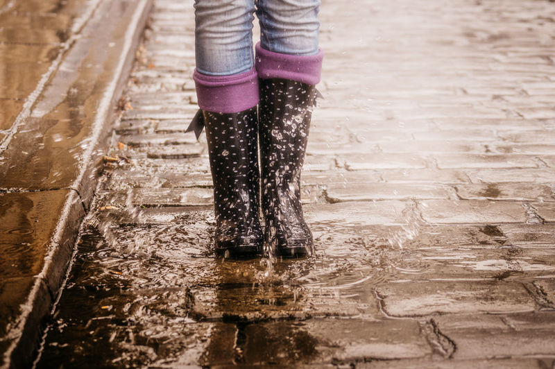 Low section of woman wearing boots while standing in puddle