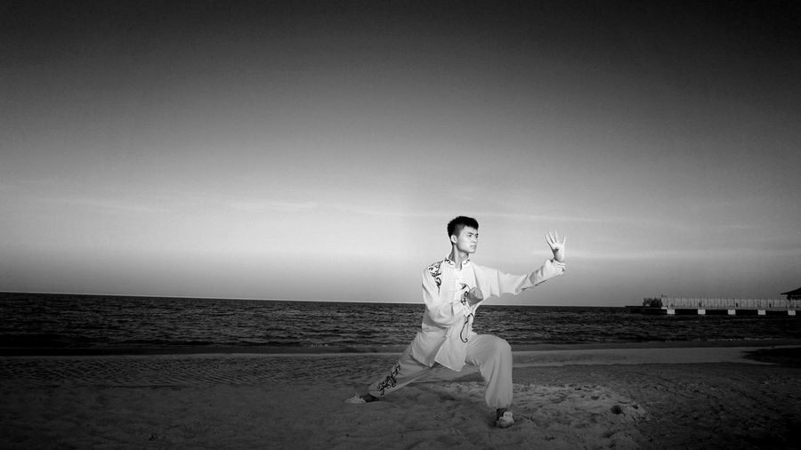 Full length of man practicing martial arts at beach against sky