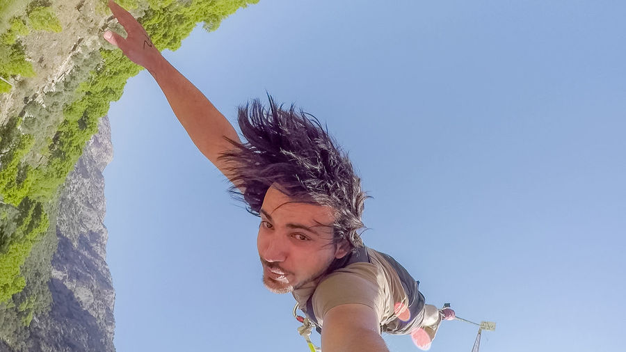 Low angle portrait of man hanging against clear sky