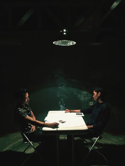 Young men holding cigarette while sitting at table in darkroom
