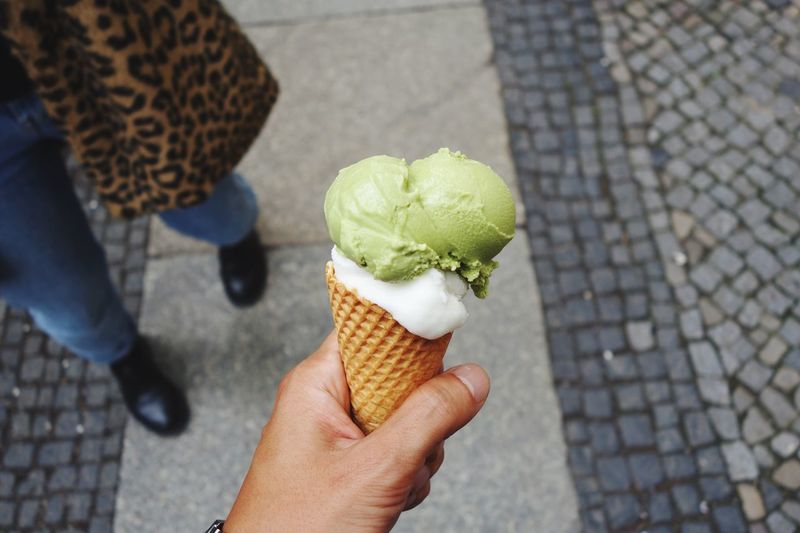 Cropped hand holding ice cream cone by woman standing on footpath