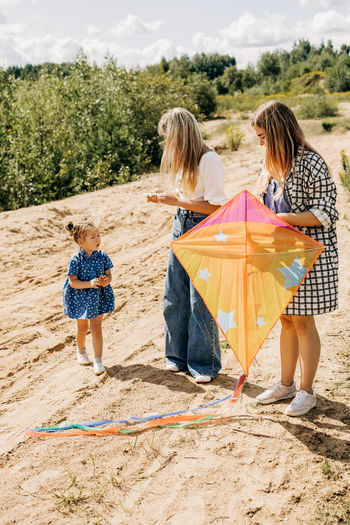 A cute little girl together with her mother and sister are preparing a kite for launch 