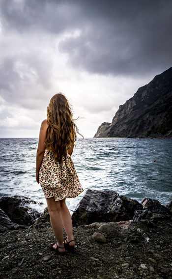 Rear view of woman standing on rock by sea against sky