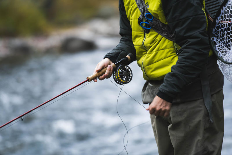 Midsection of man fly fishing at roaring fork river