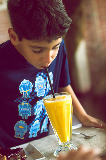 Boy drinking orange juice from straw at home