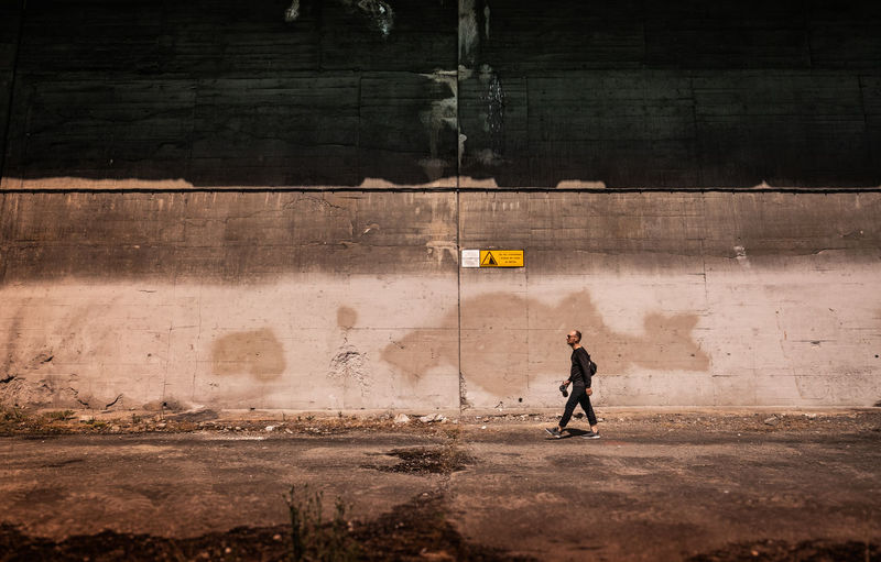 Side view full length of man walking by wall on street