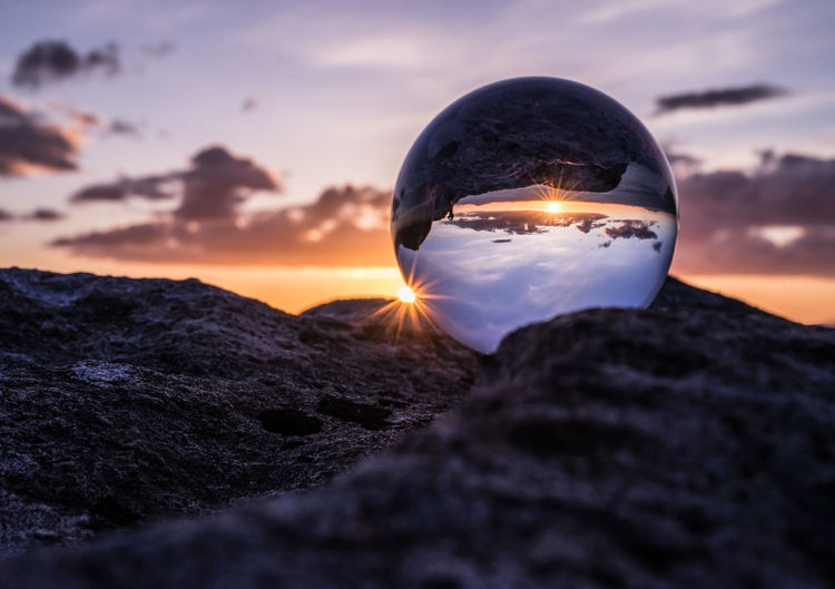 Close-up of crystal ball on rock against sky during sunset