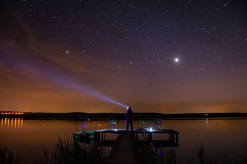 Full length of man holding flashlight by lake at night
