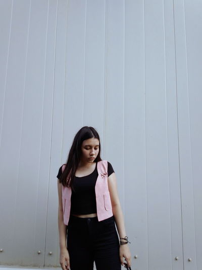 Young woman looking down while standing against wall