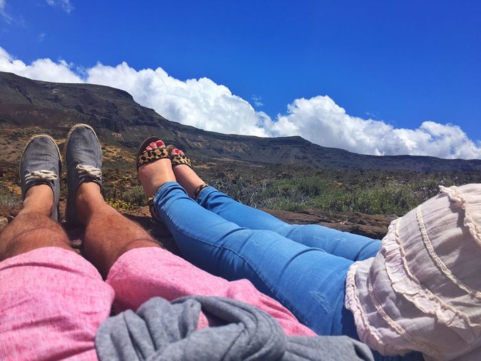 Low section of couple relaxing on field against mountain
