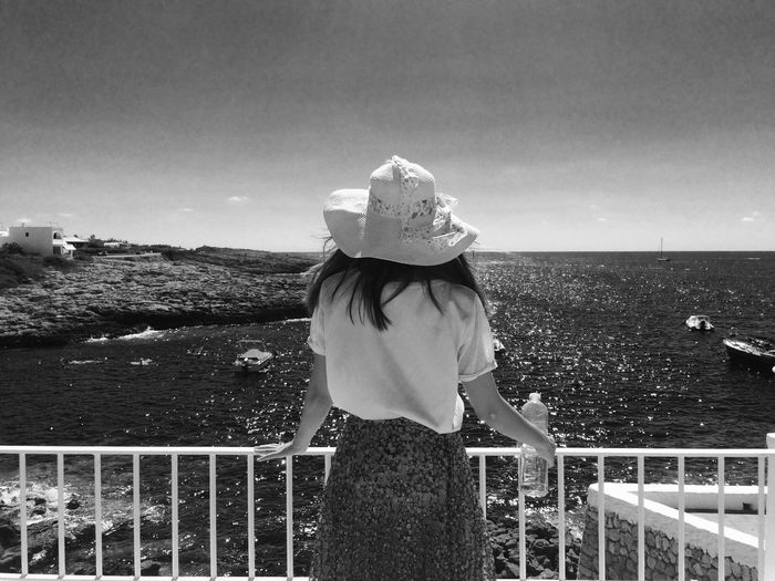 Rear view of woman standing at railing by sea against clear sky