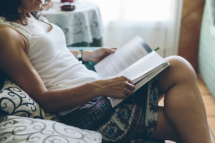 Midsection of woman reading book while sitting on sofa at home