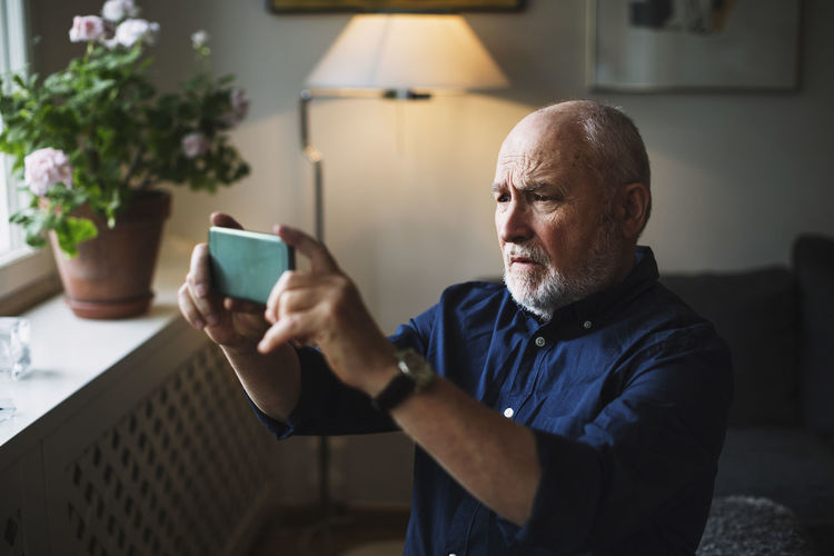 Senior man photographing through mobile phone at home