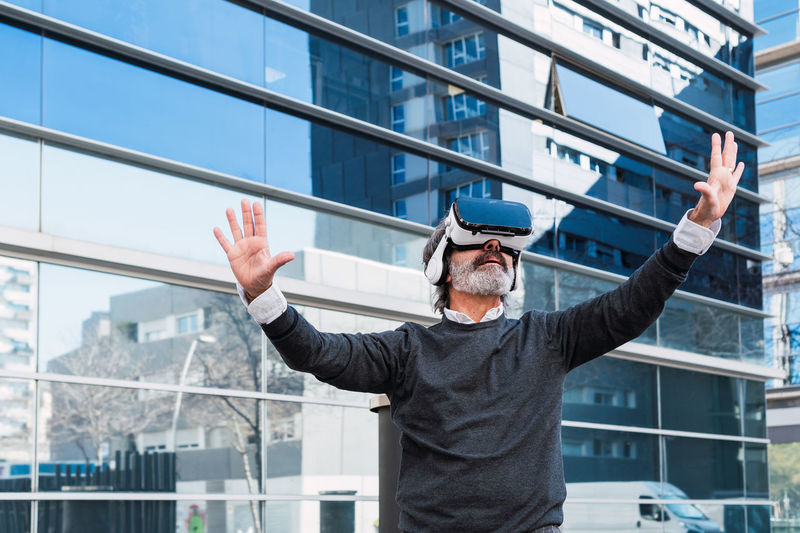 Amazed senior man using vr headset outdoor the office building, modern technologies experience