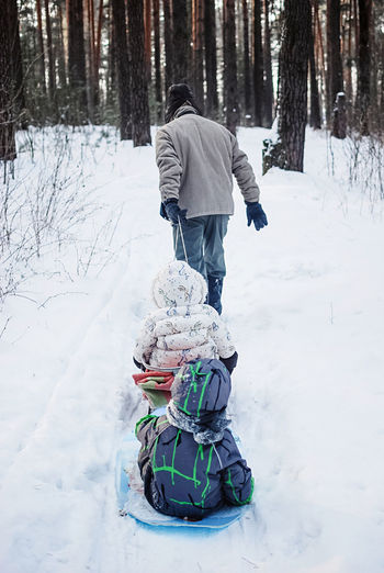 Rear view of grandfather with two grandkids in snow forest