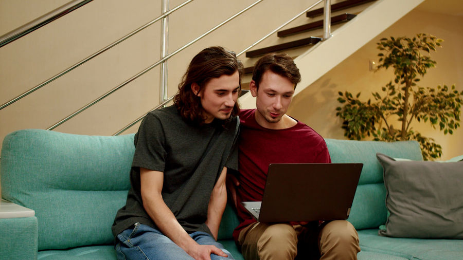 Gay couple using laptop while sitting on sofa at home