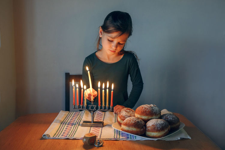 Girl lighting candles on a menorah for traditional winter jewish hanukkah holiday at home. 