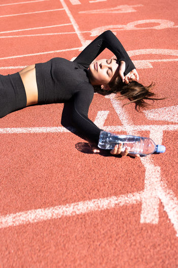 High angle view of tired woman lying with water bottle on running track