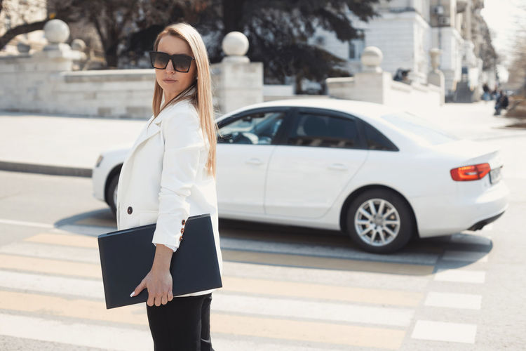 Woman wearing sunglasses standing against car in city