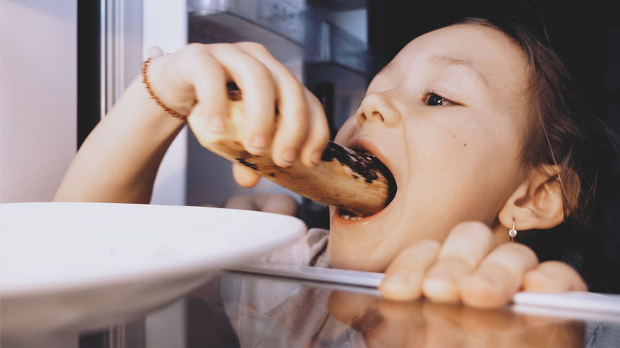 Close-up of girl eating food from refrigerator