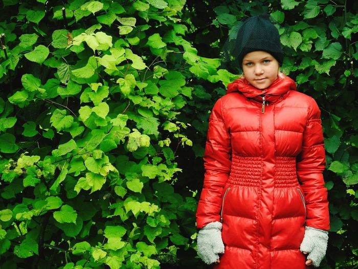 Portrait of girl in red jacket standing against plants