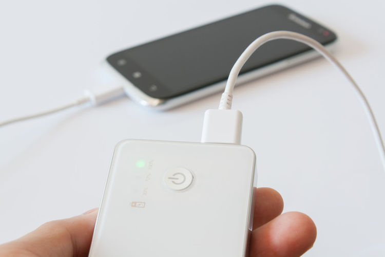Cropped hand holding portable charger against white background