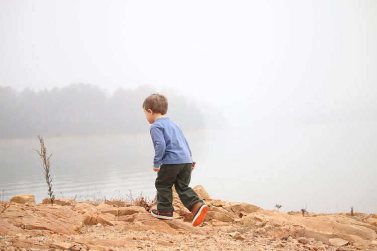 Rear view of boy standing on lake against clear sky