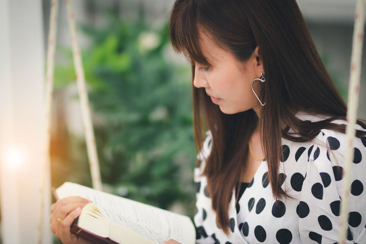 Close-up of young woman reading book while sitting outdoors