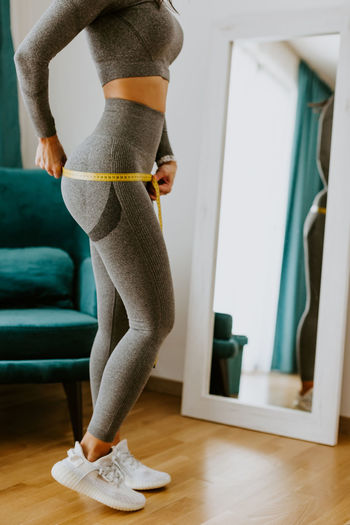 Low section of woman measuring buttocks with tape measure