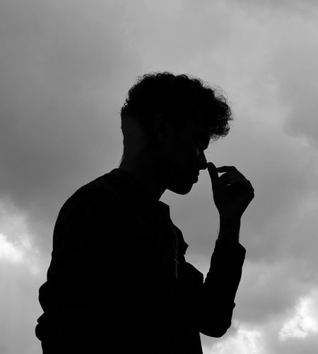 Silhouette man smoking cigarette against sky