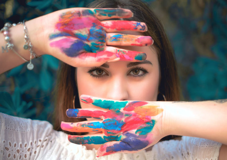 Close-up portrait of young woman covering mouth with colored hand