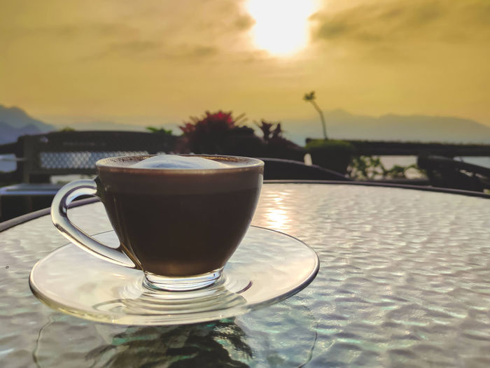 Close-up of coffee on table by swimming pool against sky during sunset