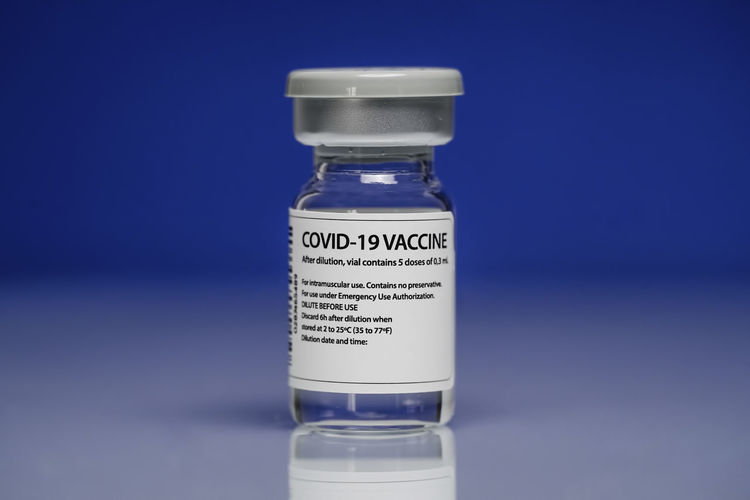 Medical glass vial with coronavirus vaccine placed against blue background